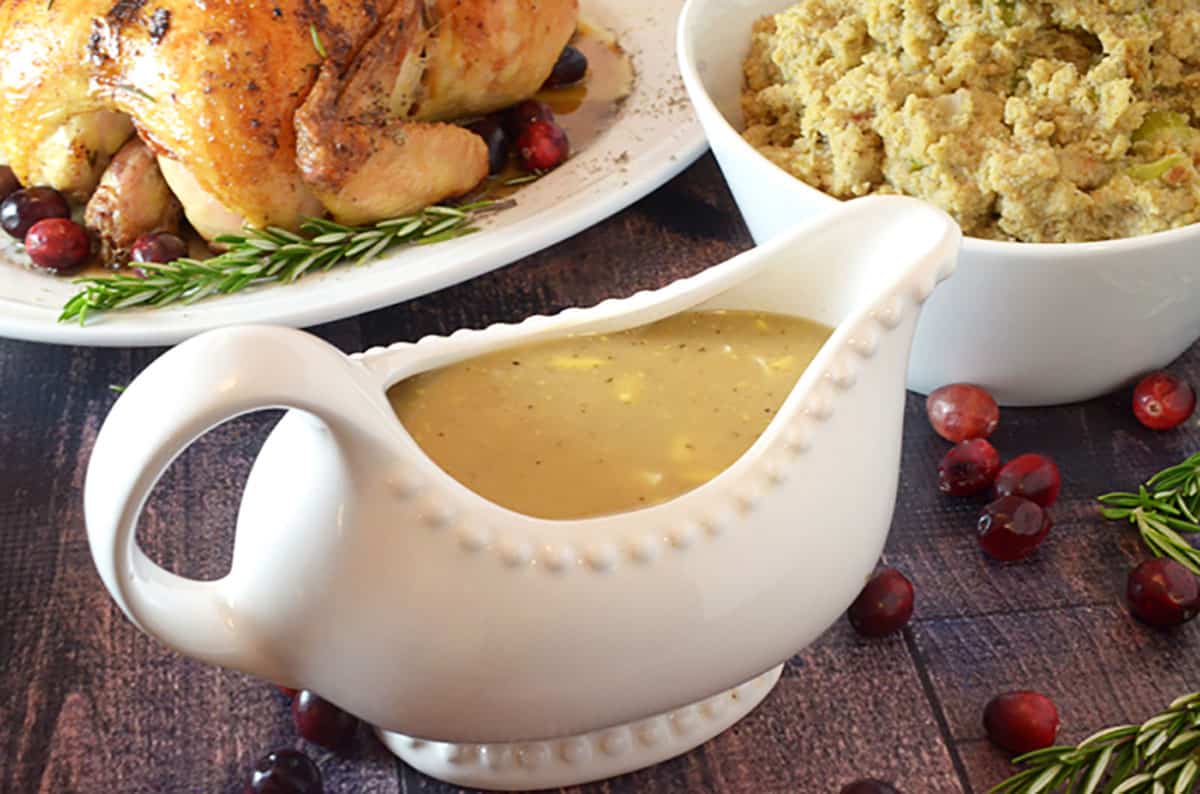 A filled gravy bowl with a bowl of stuffing and a roasted chicken.