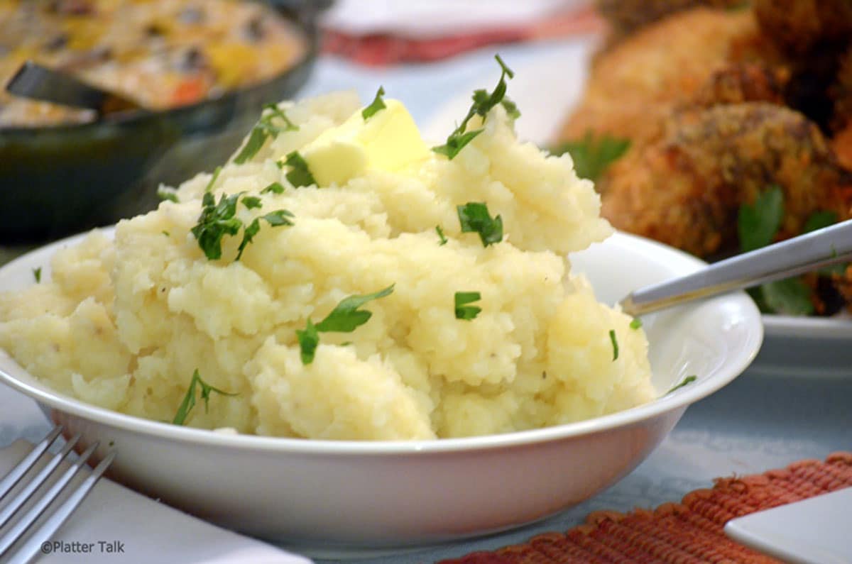 Closeup of bowl of mashed potatoes garnished with parsley.
