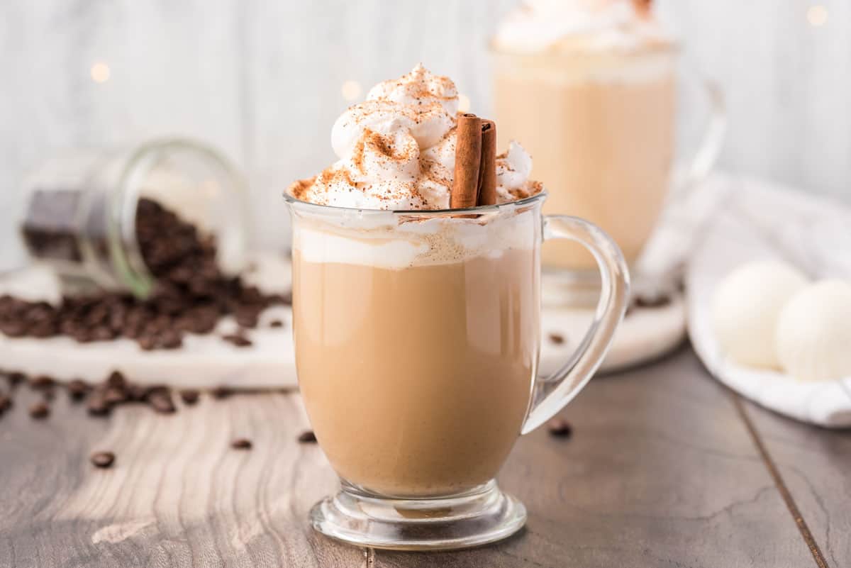 A mug of eggnog latte with coffee beans in the background