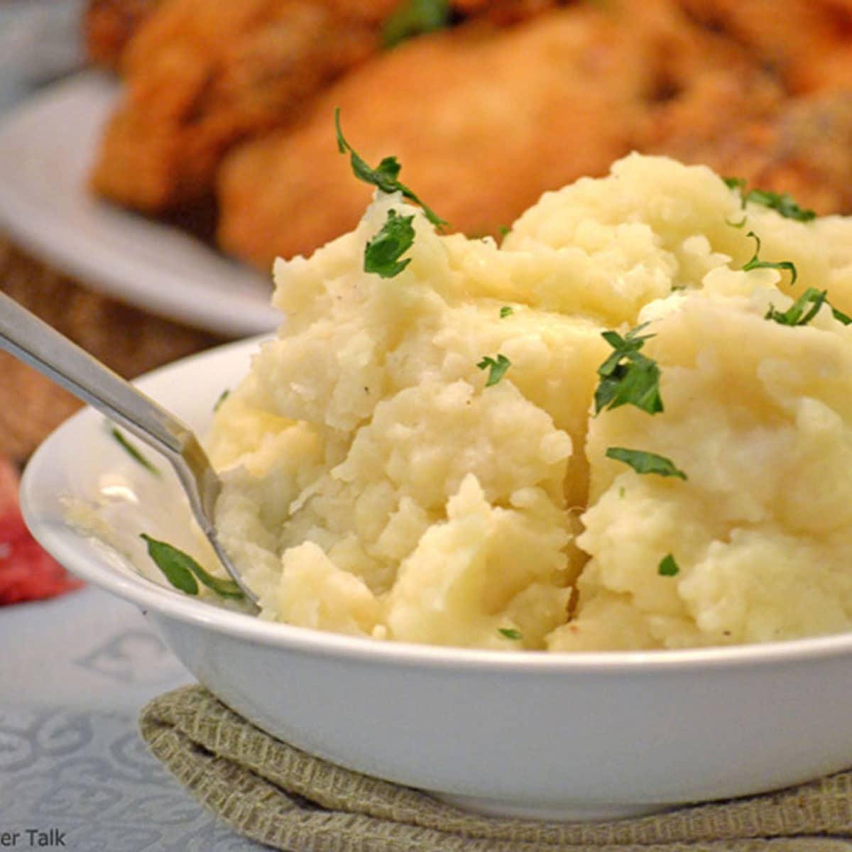 A close-up of a bowl of mashed potatoes with fried chicken in the background.