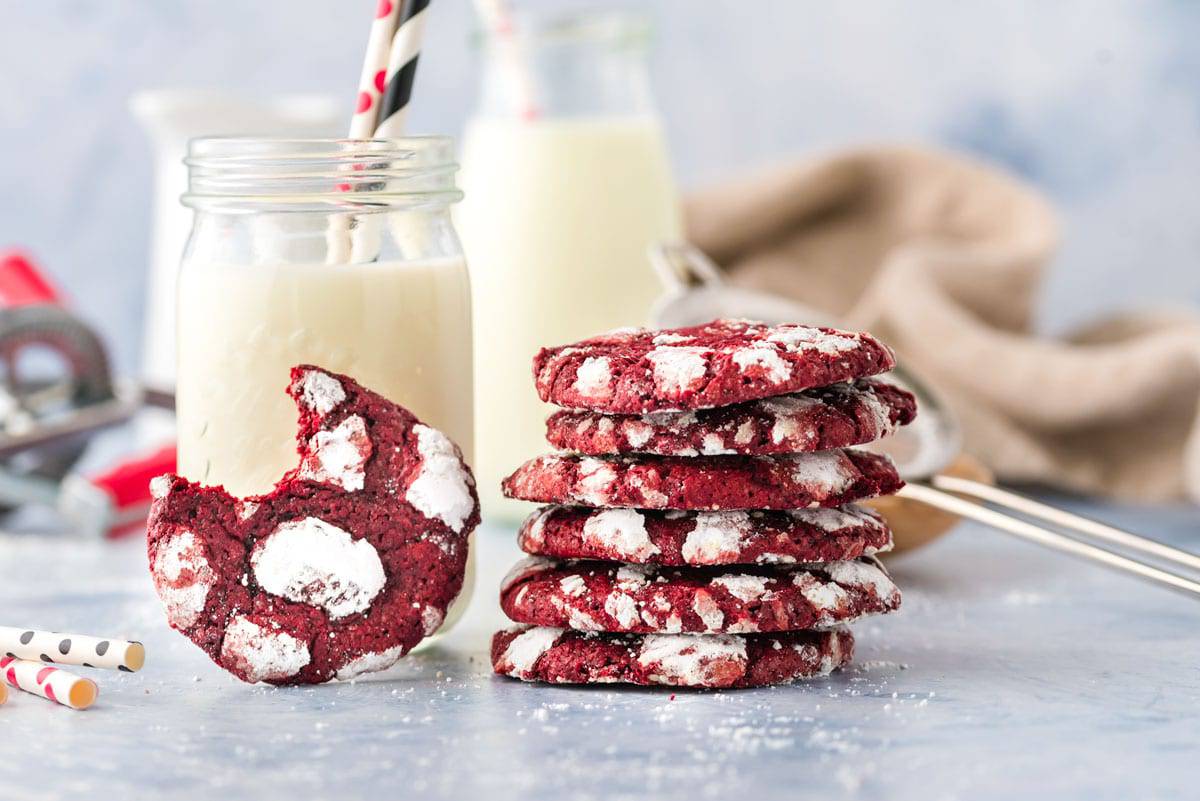 A stack of red velvet crinkle cookies in front of a jar of milk
