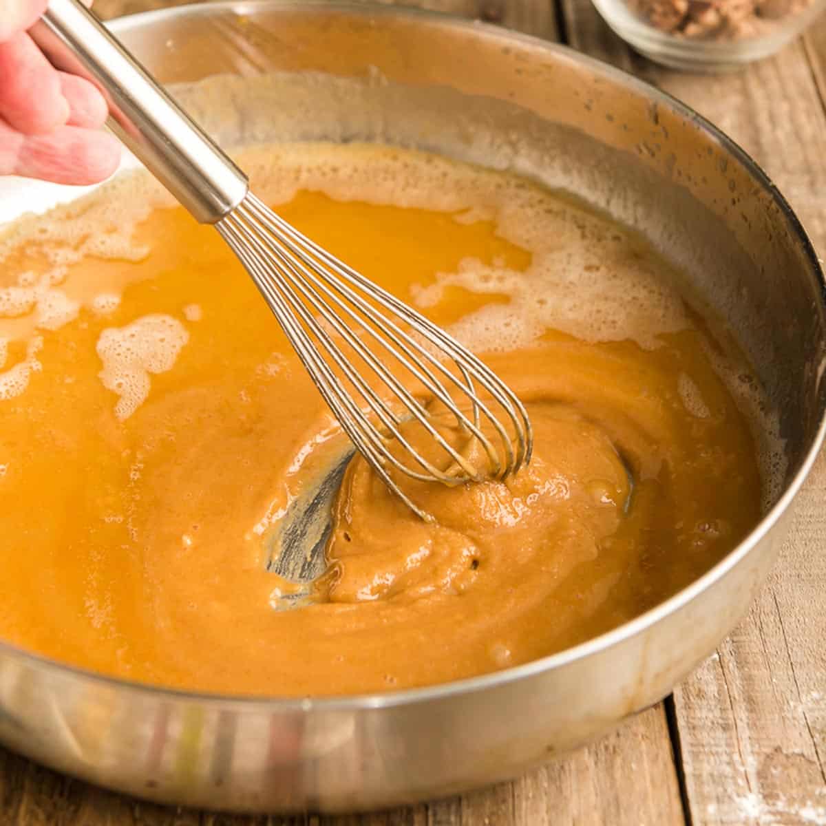 A whisk stirring a roux in a skillet.
