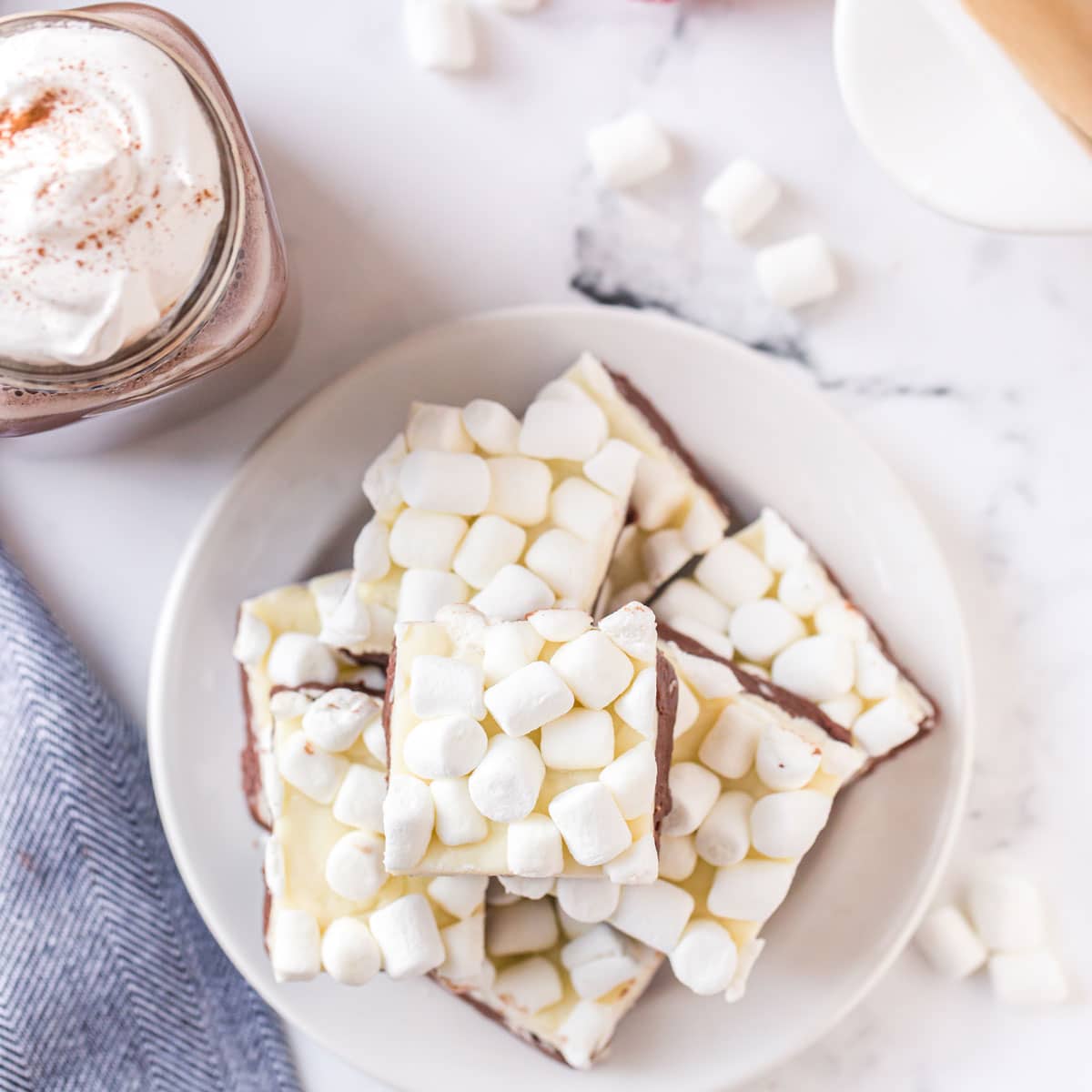 A plate of hot chocoalte fudge covered with mini-marshmallows. A plate of marshmallow-covered fudge with glass of hot chocolate.