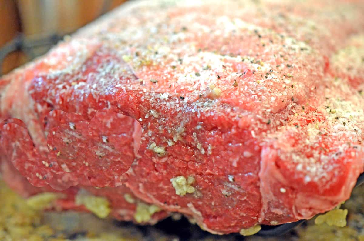 An uncooked hunk of beef, covered with garlic, salt, and pepper.
