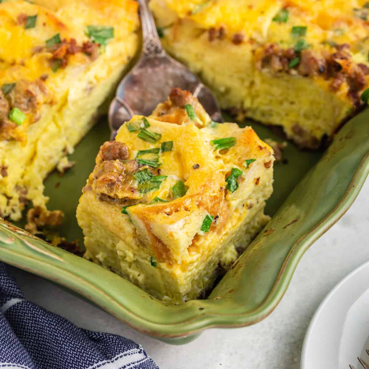 Cutting a portion of breakfast casserole in a green baking dish.