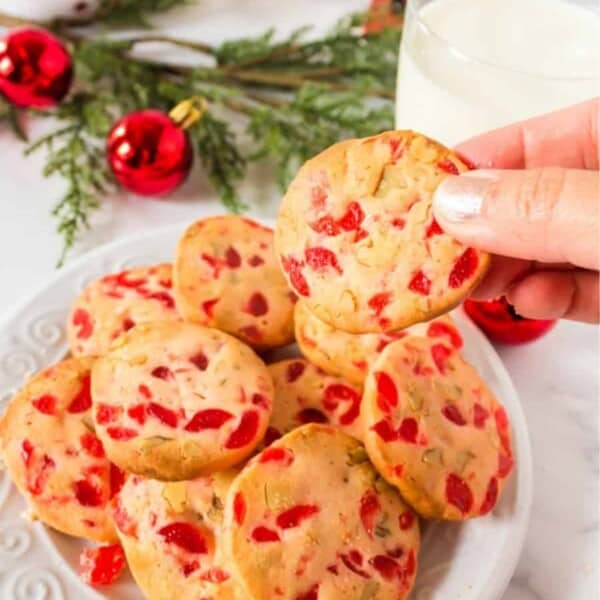 A plate of Christmas cookies with ornaments and glass of milk in the background.