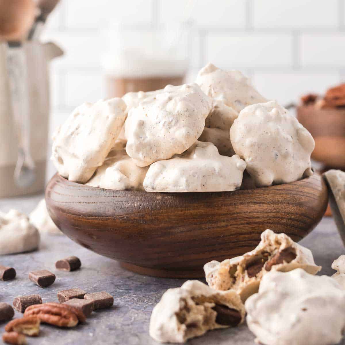 A wooden bowl filled with forgotten cookies with chocolate chips and pecans strewn about.