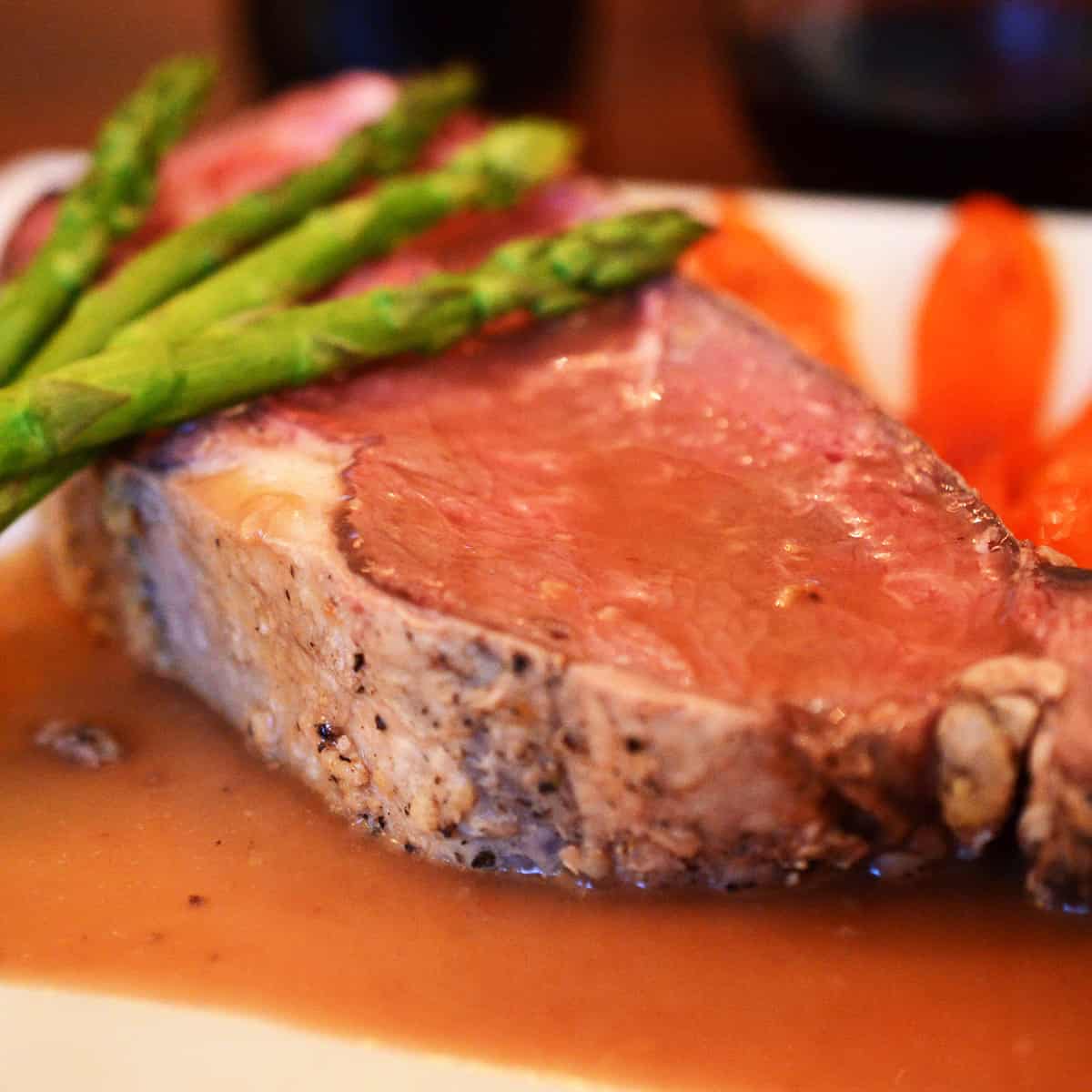 A plate of medium-rare prime rib with asparagus and carrots.