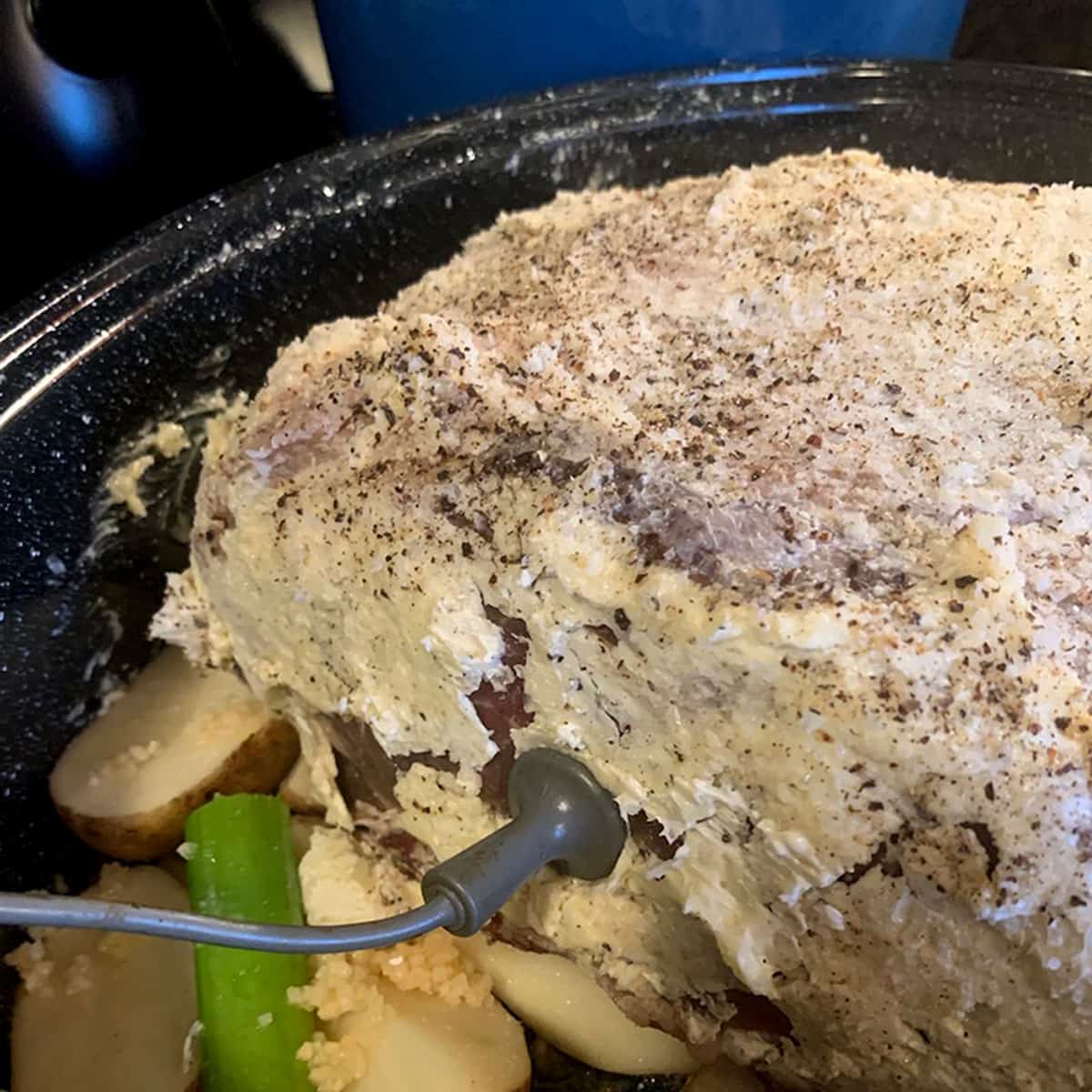 A prime rib rubbed in butter. An uncooked piece of meat rubbed in butter with a temperature probe stuck in it.