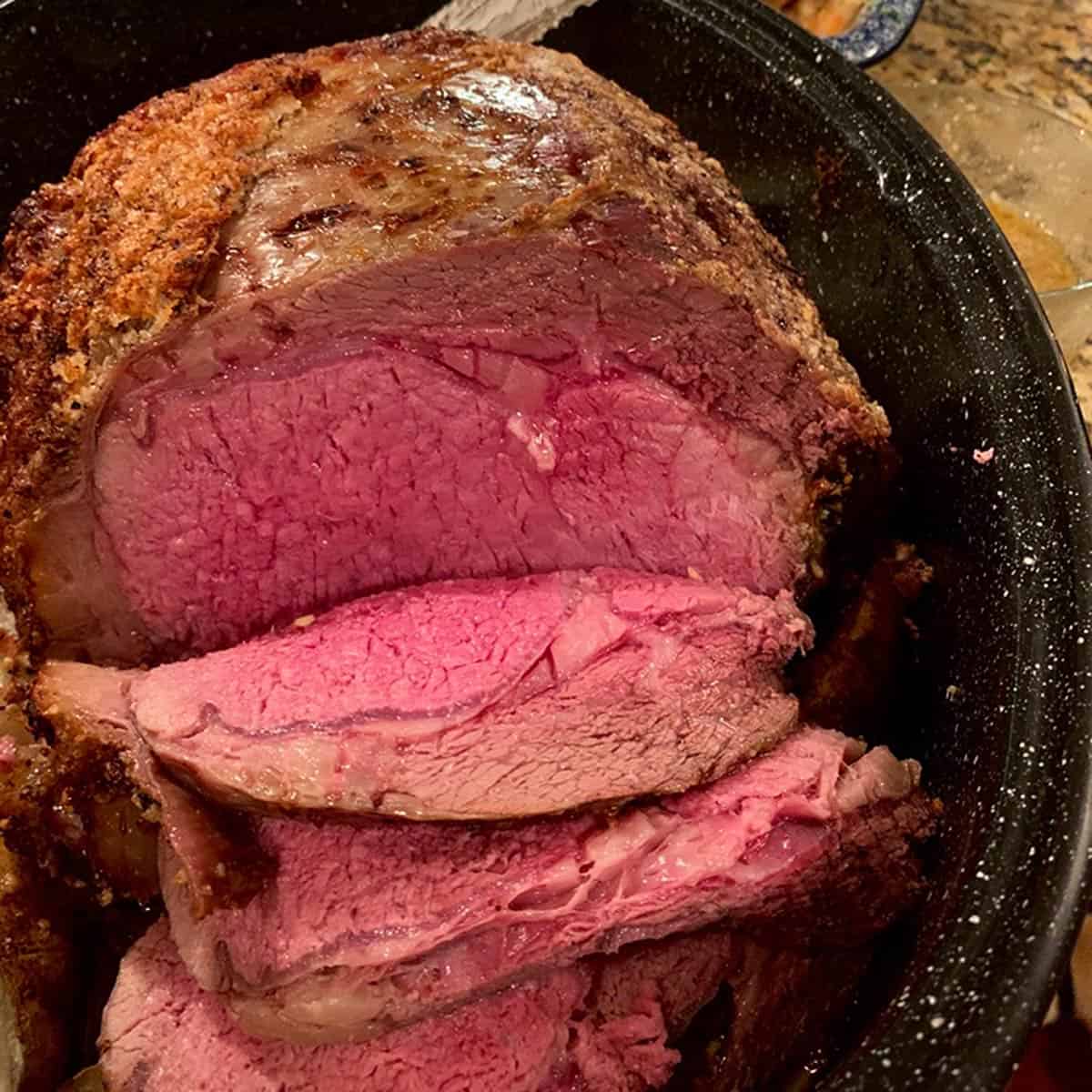 A boneless prime rib of beef roasted to medium-rare, in a roaster.