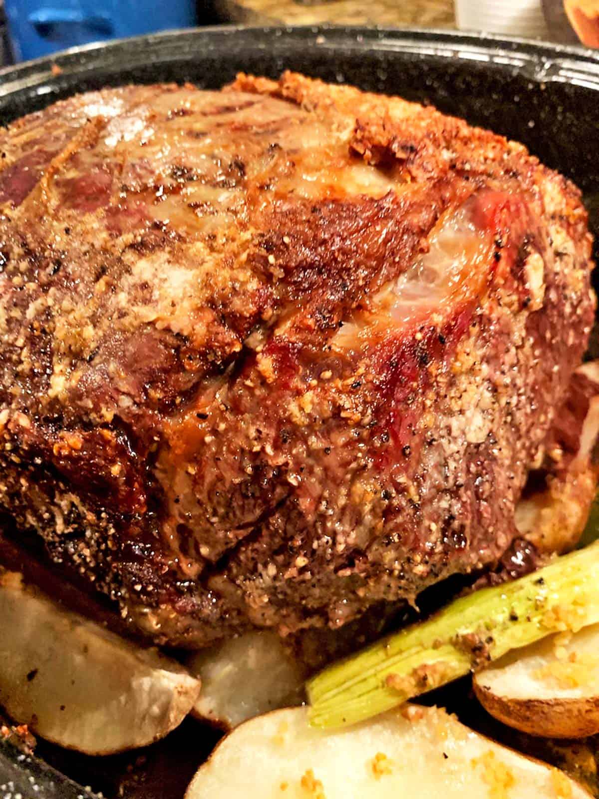 A prime rib fresh out of the oven. A finished beef roast sitting in a roaster on top of celery and potatoes.