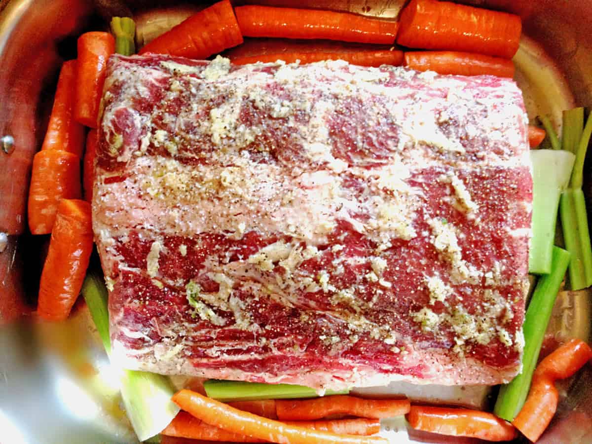 A seasoned, uncooked beef roast sitting in a roaster with carrots and celery.