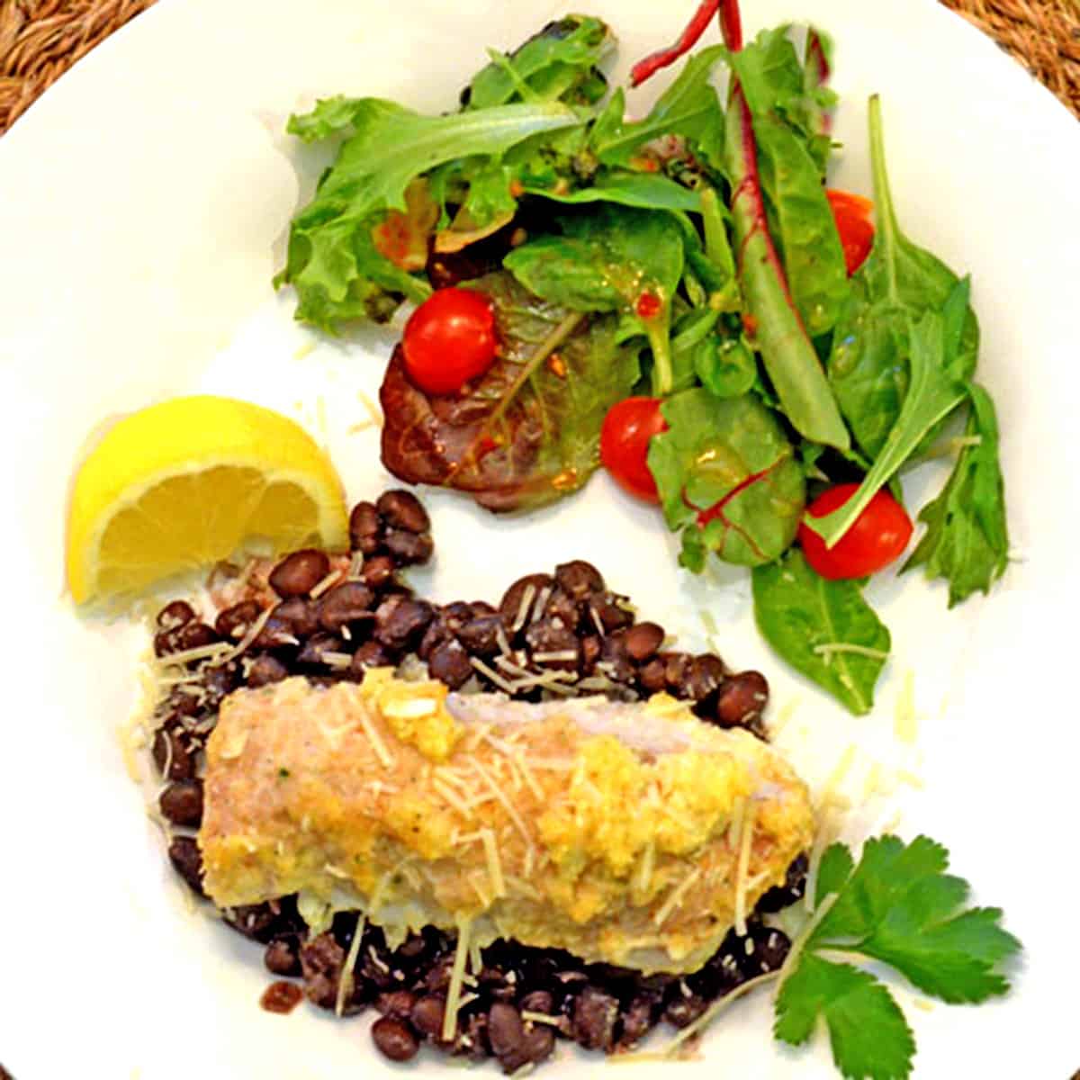 A dinner plate with fish over black beans and a salad.