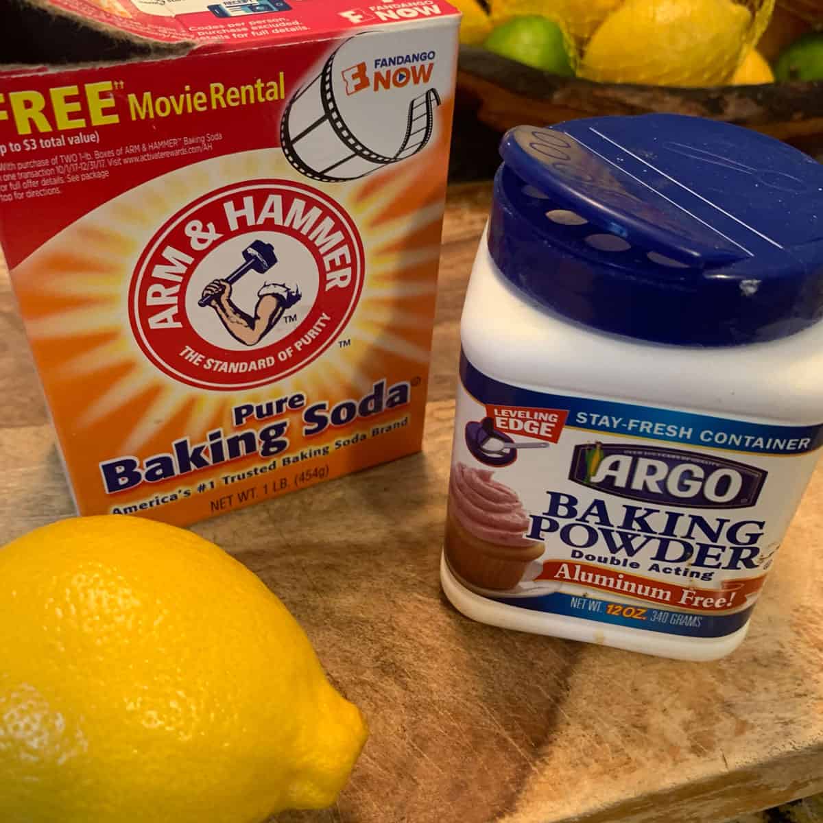 A compariso. of bakign soda and baking powder. A box of baking soda with some baking powder and a lemon.
