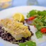 a plate of baked fish over black beans and green salad