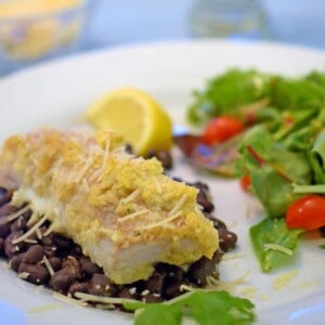 a plate of baked fish over black beans and green salad