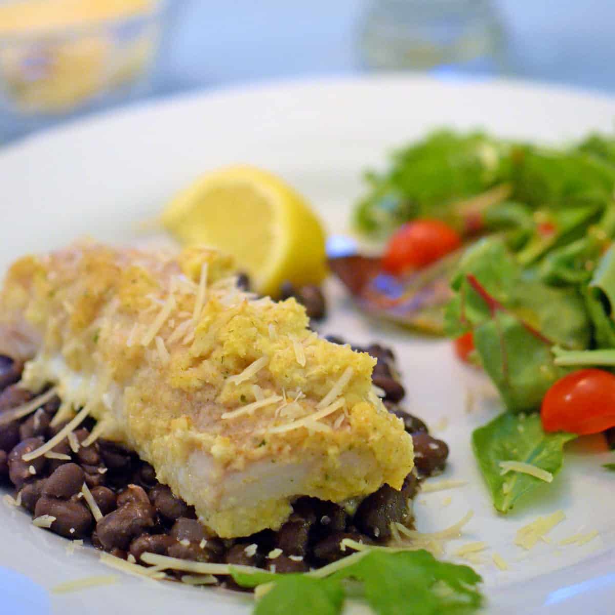 A plate of food with whitefish and black beans and green salad.