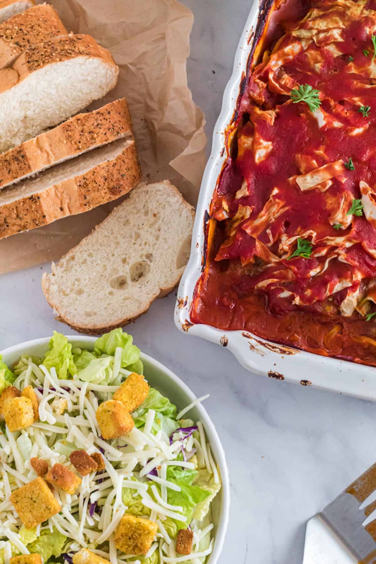 Overhead view of a casserole with salad and rolls.