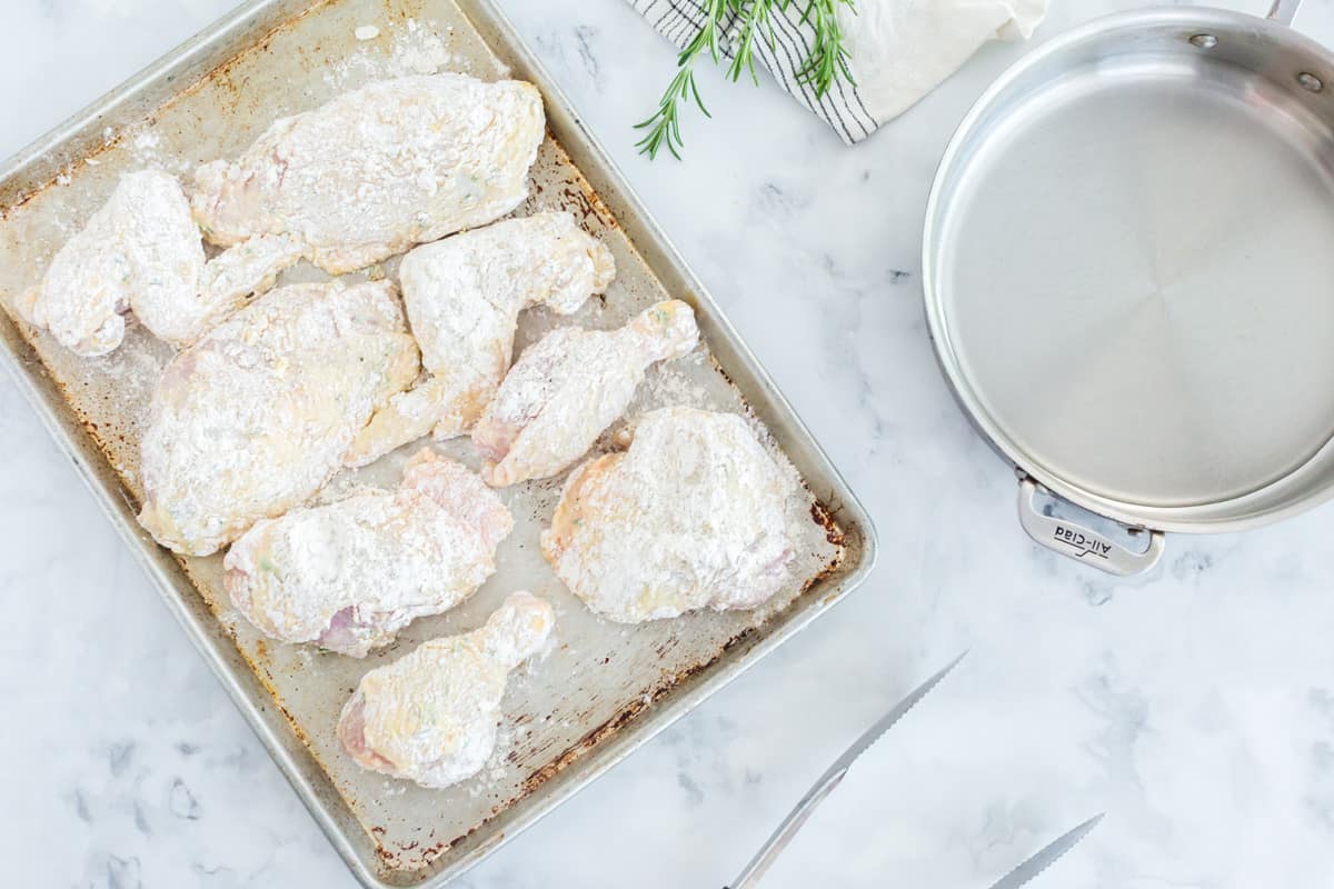 A bunch of chicken covered with flour and sitting on a baking pan.