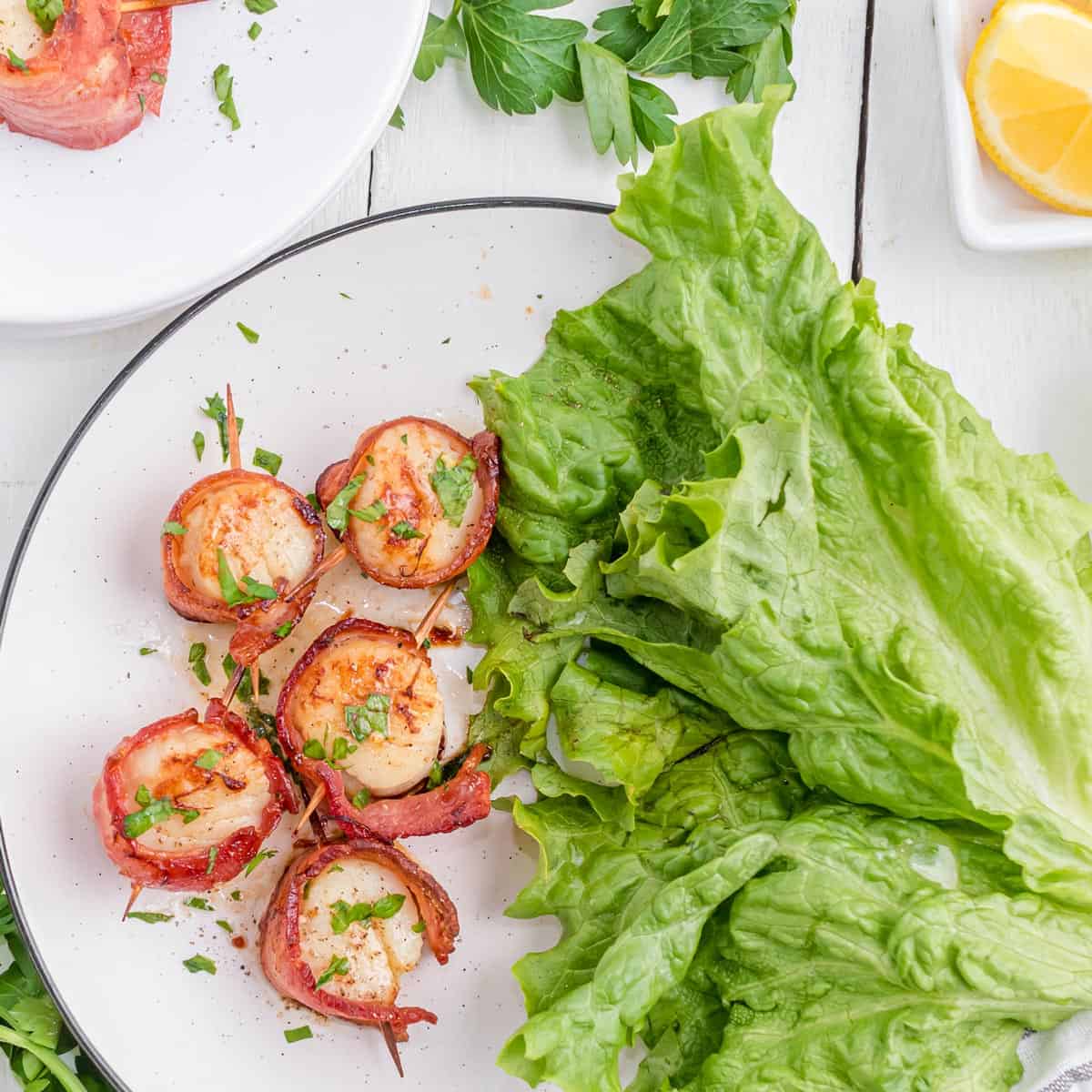 A serving plate of bacon-wrapped scallops with a big leaf of lettuce.