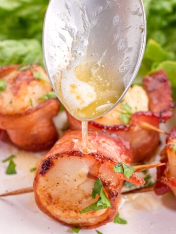 Melted butter being drizzled over air fried bacon wrapped scallps.