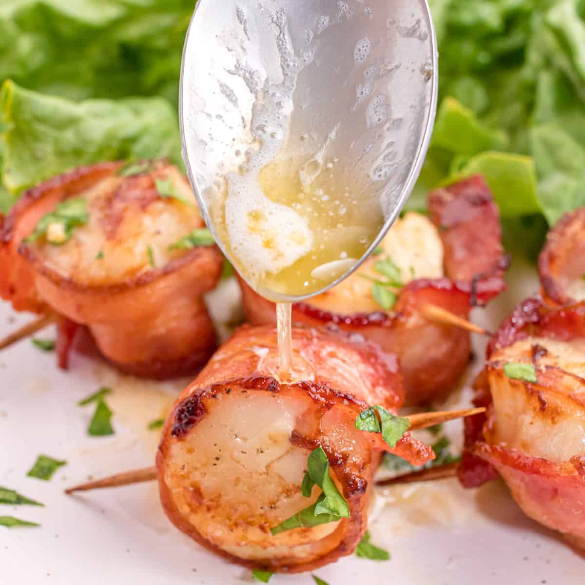 Melted butter being drizzled over air fried bacon wrapped scallps.