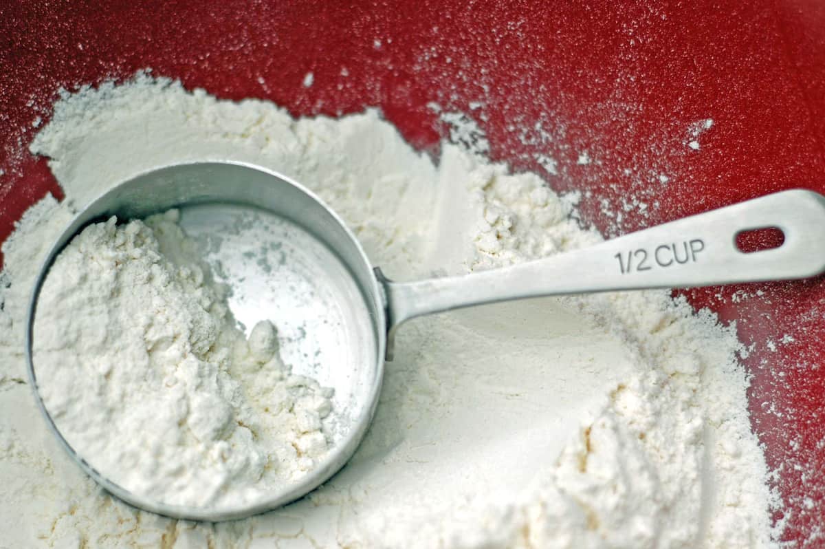 A measuring cup in a bowl of flour.