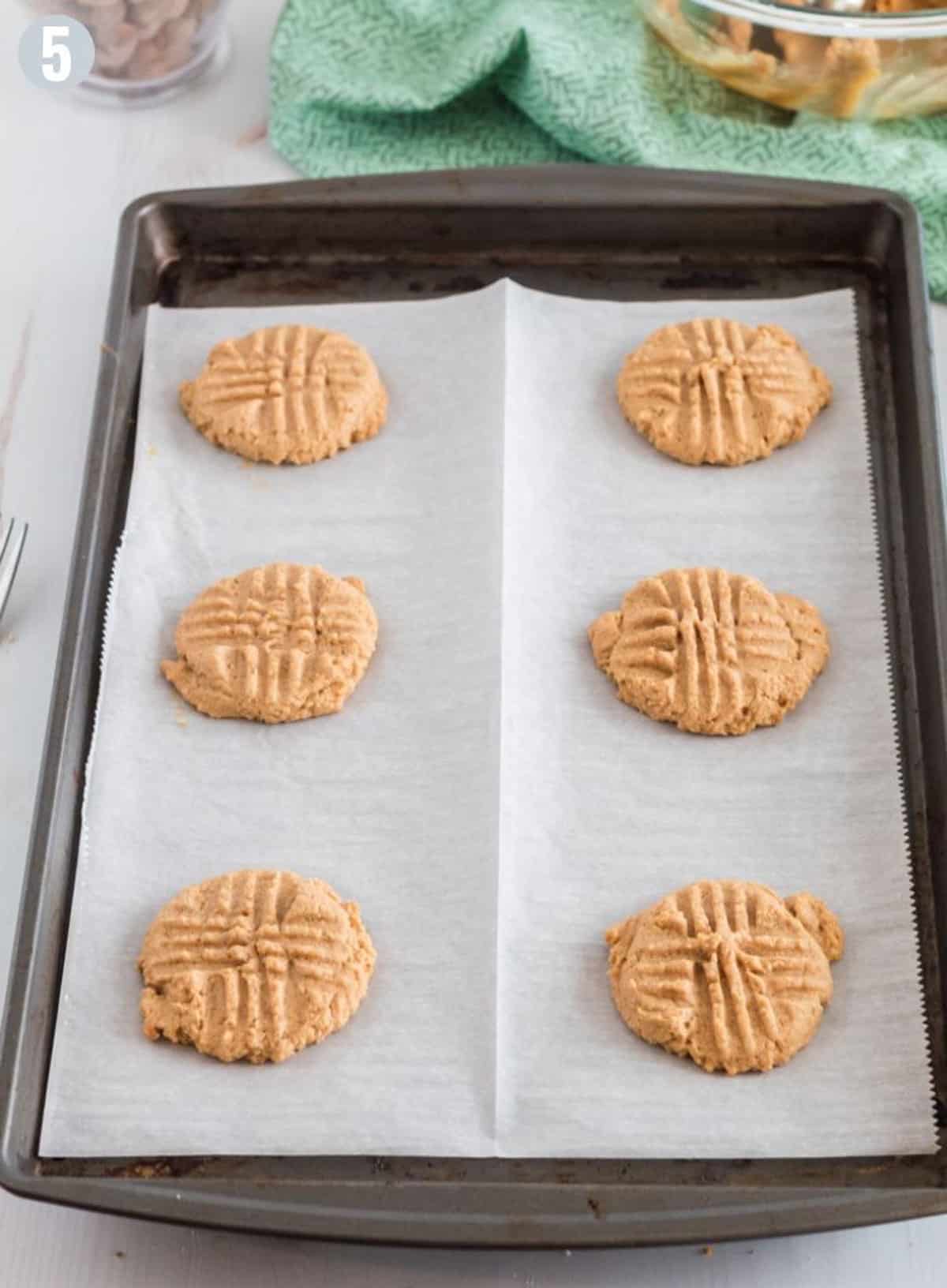 A cookie sheet lined with parchment paper and some cookies on it.