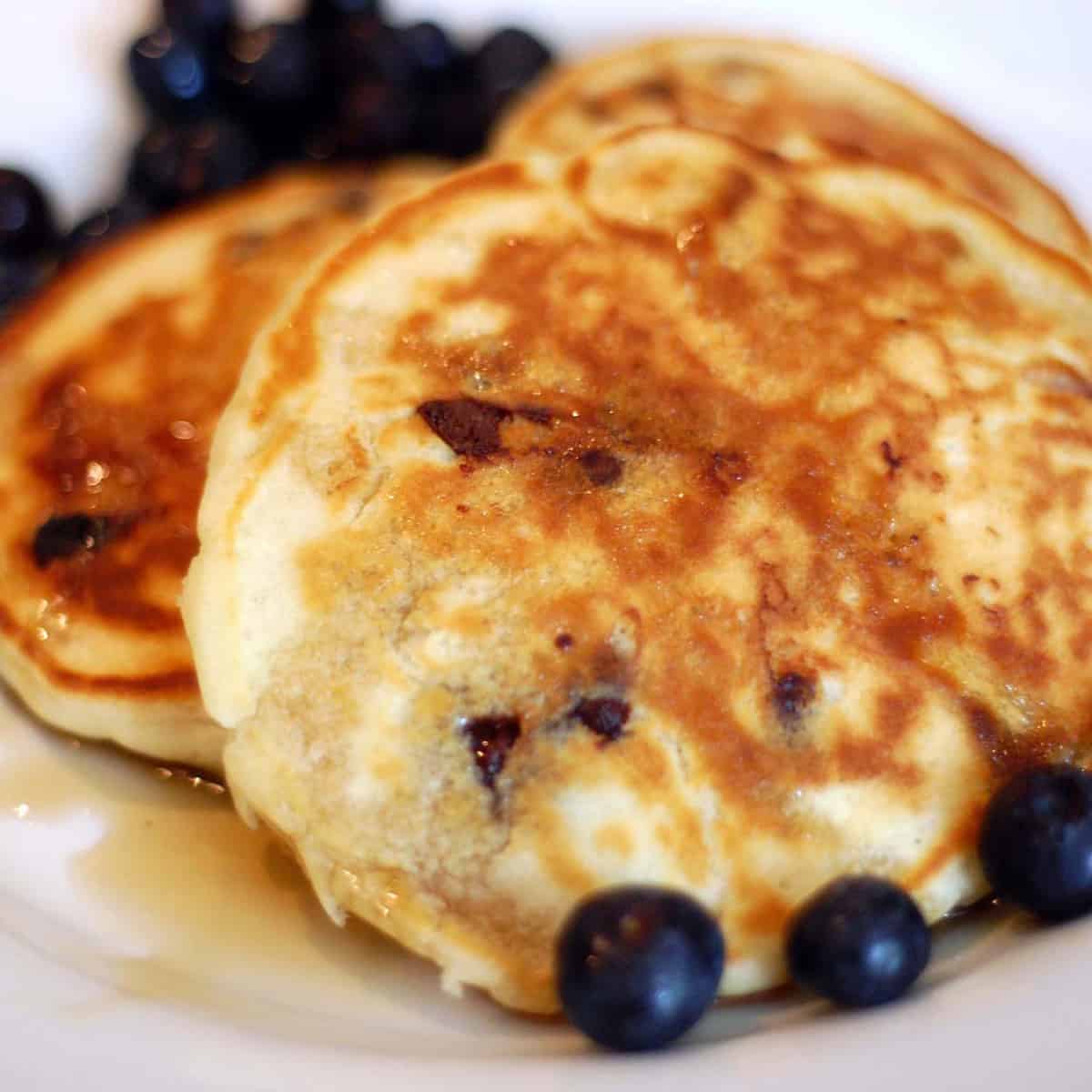 close-up of homemade pancakes with blueberries and syrup on a plate.