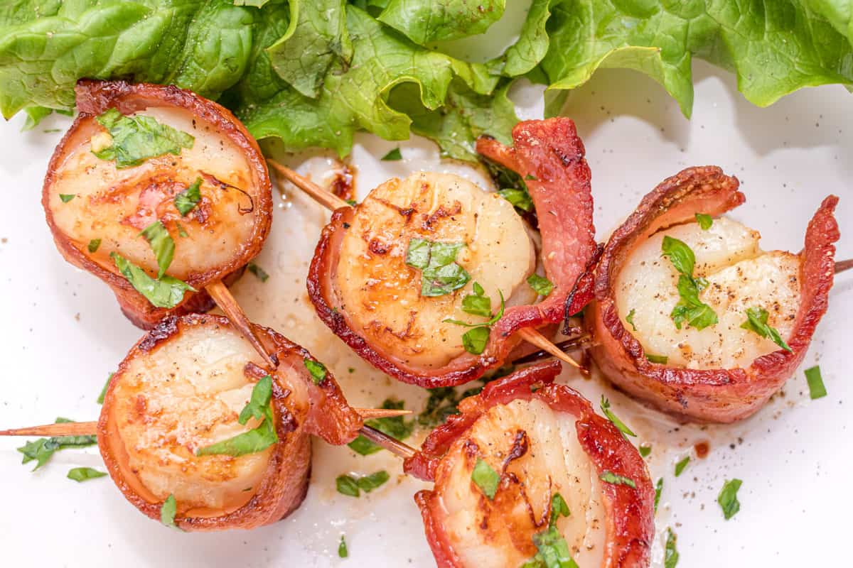 A plate of bacon-wrapped scallops garnished with chopped parsley.