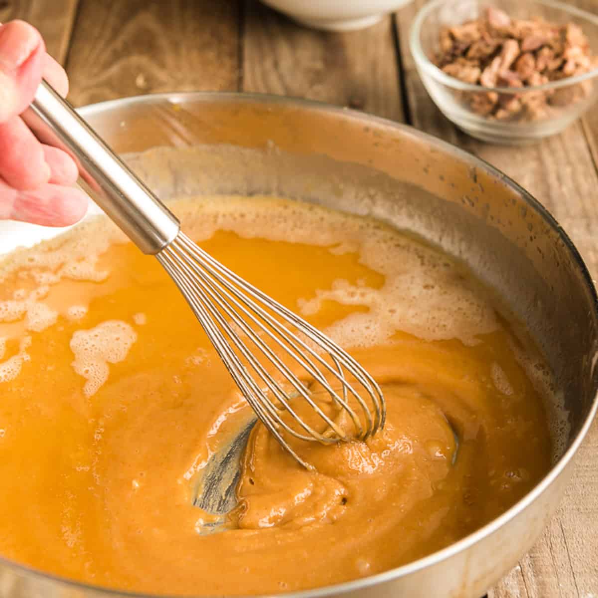Using a whisk to stir a brown roux in a pan.