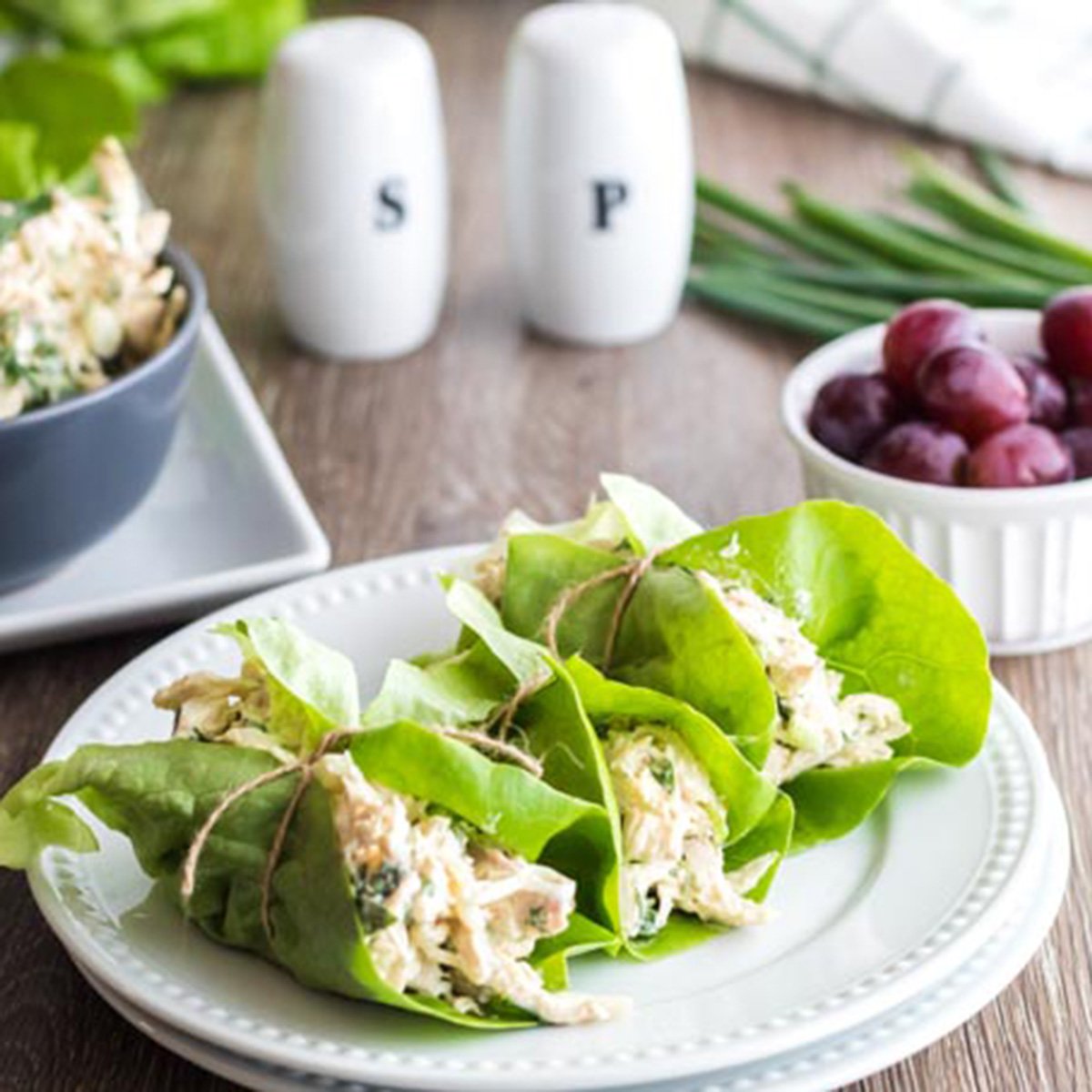 A plate of chicken salad wraps and a dish of grapes.