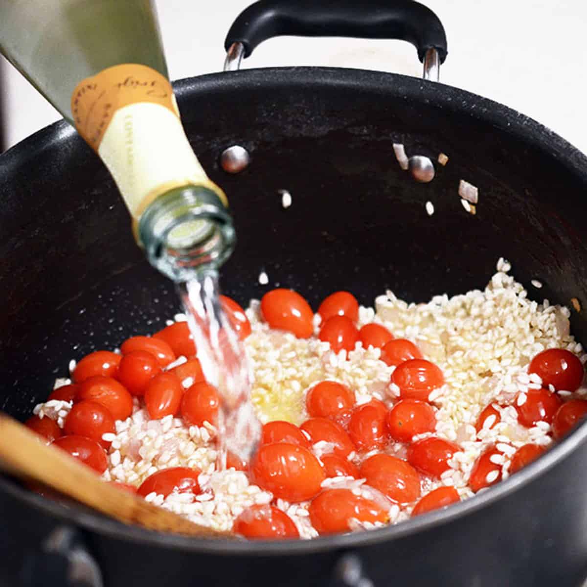 Adding white wine to risotto and tomatoes.