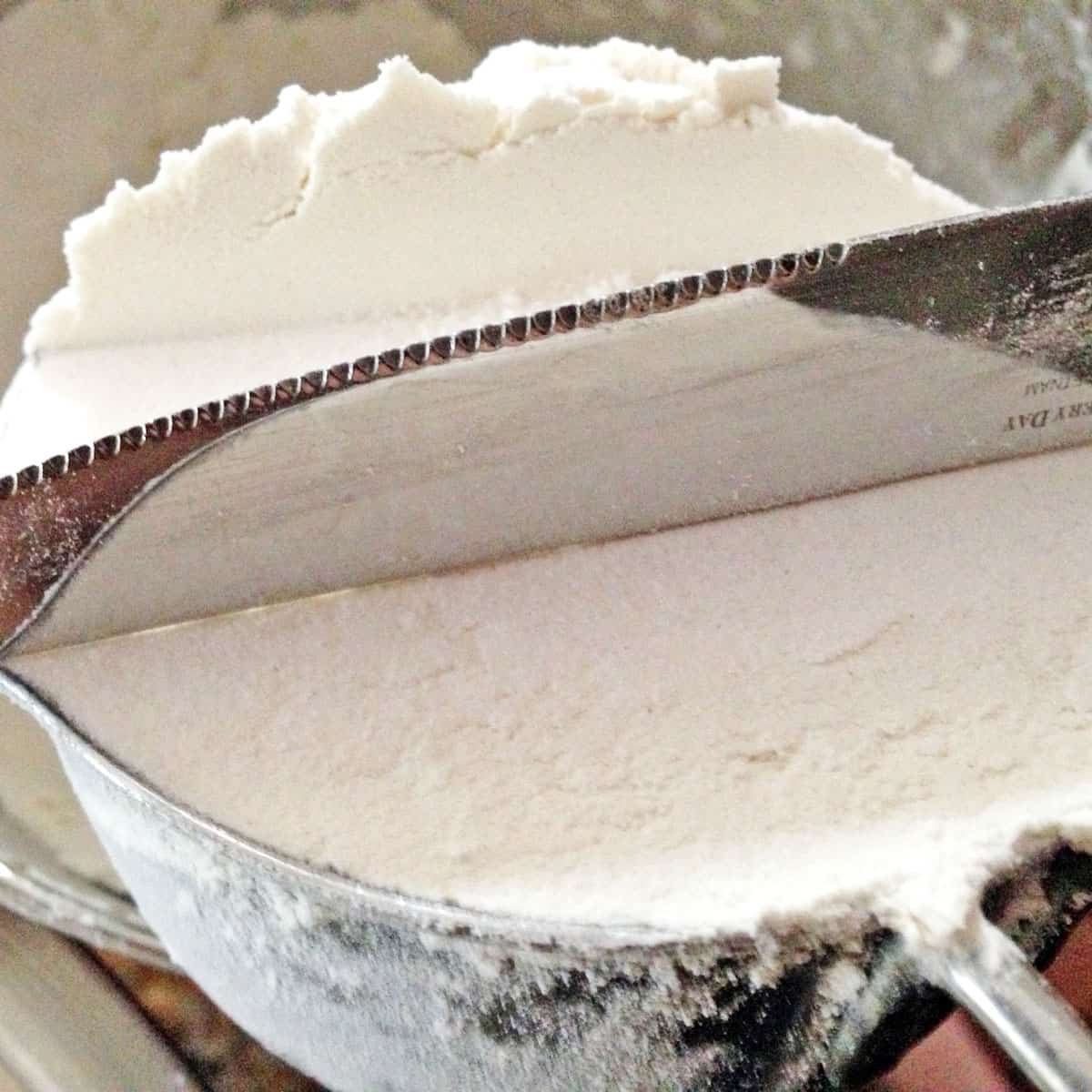 Measuring flour in a measuring a cup and leveling it off with a table knife.