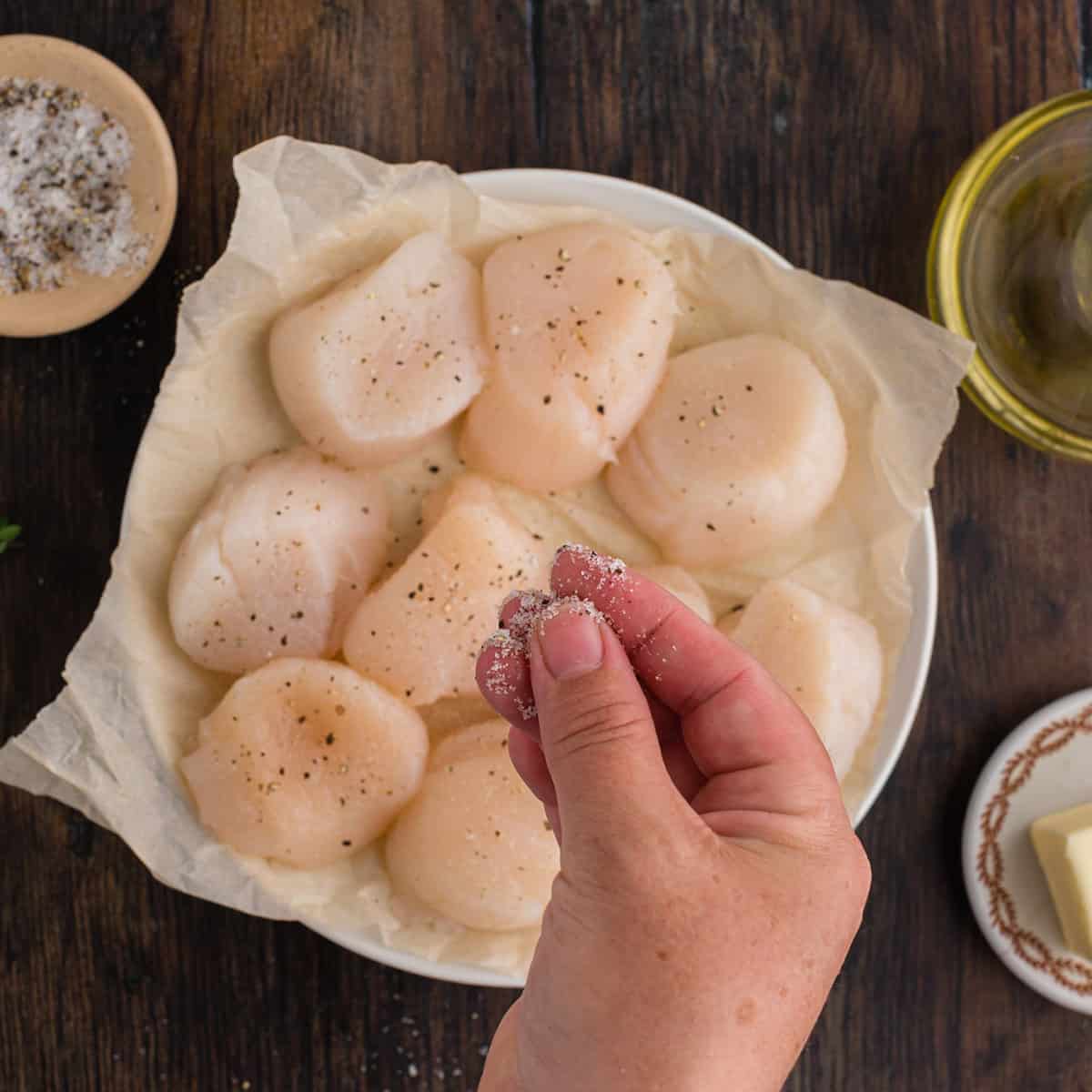 Adding salt and pepper to some uncooked seafood sitting in a bowl.