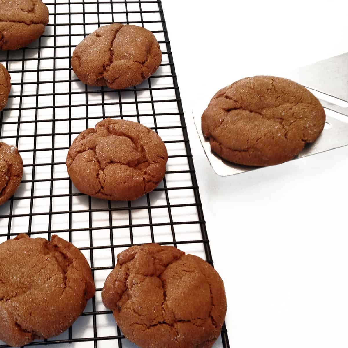 Molasses cookies being placed on a cooling rack, using a spatula.