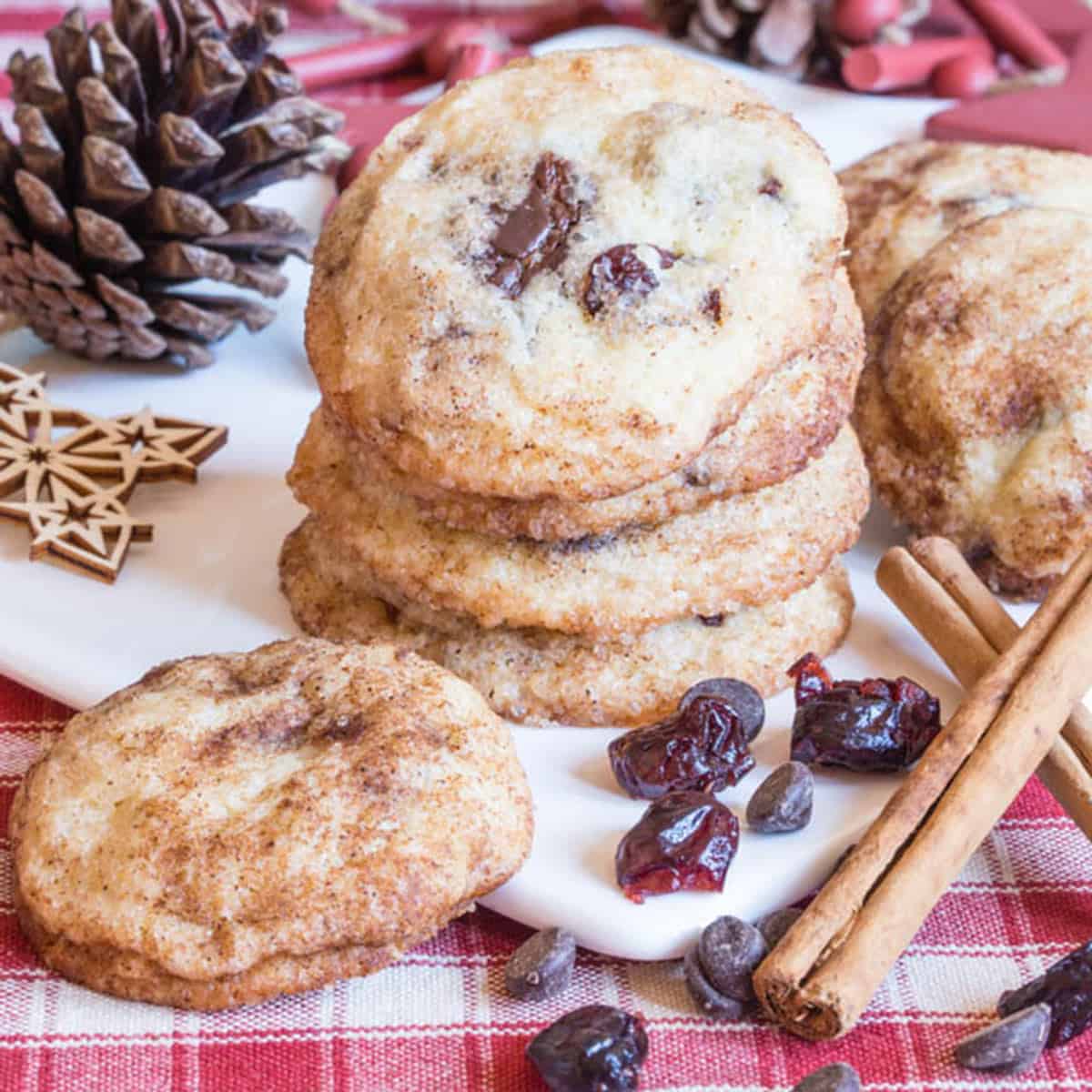 A stack of cookies next to a pine cone with cinnamon sticks.