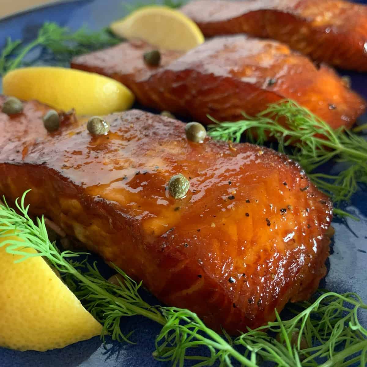 A bunch of salmon pieces garnished with fresh dill, lemons, and capers.