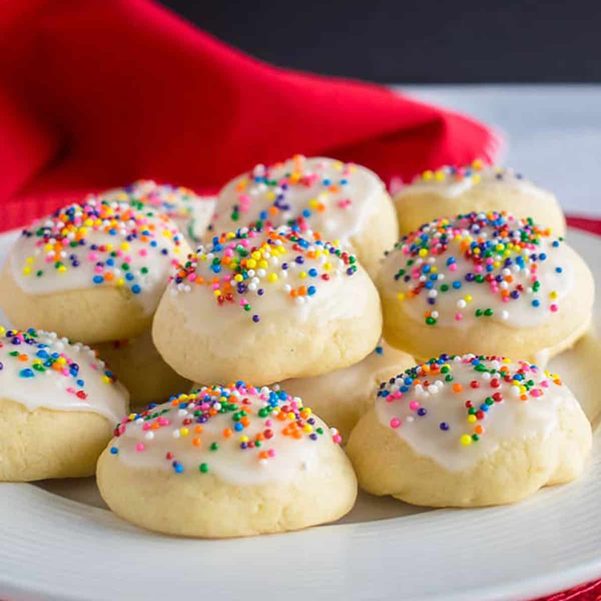 A plate of small round cookies with vanilla icing and colored sprinkles.