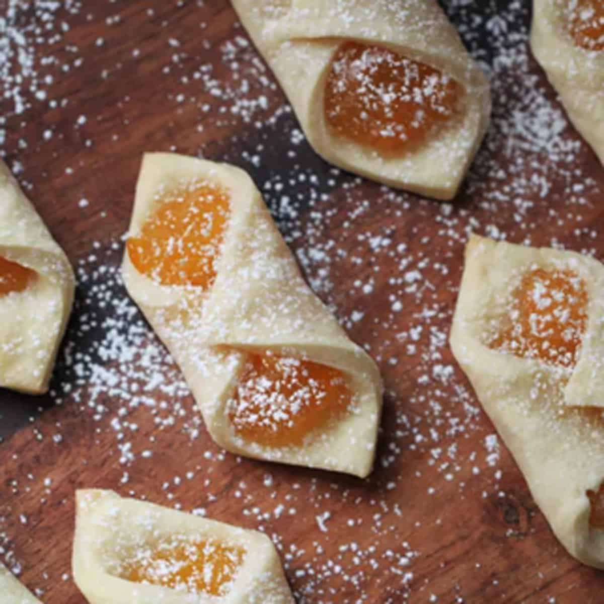 A bunch of pastries on a  wood board, sprinkled with powdered sugar.