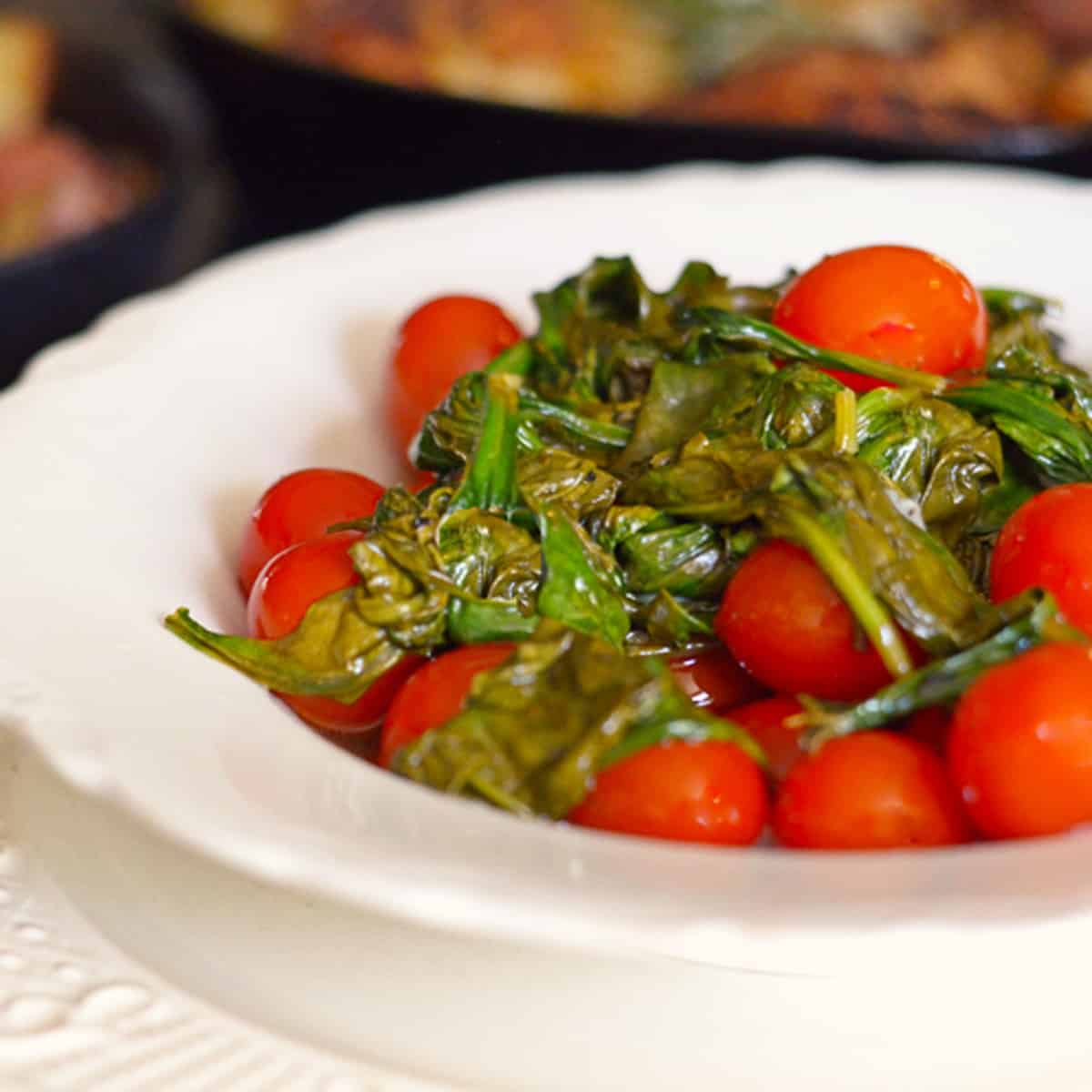 A bowl of wilted spinach and roasted tomatoes.
