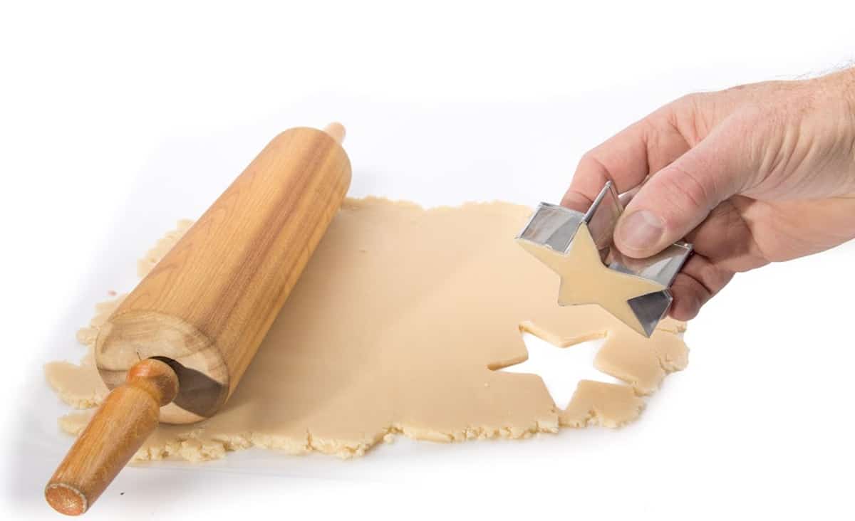 A cookie cutter cutting out some dough with dough and a rolling pin.