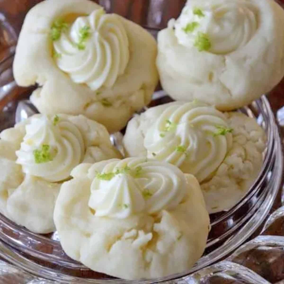 A platter full of white shortbread cookies topped with cream cheese and lime zest.