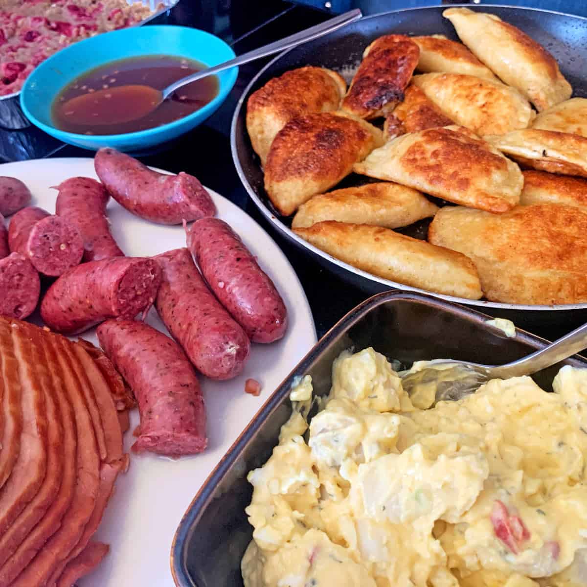 A pan of pierogies with Polish sausage and potato salad and ham.