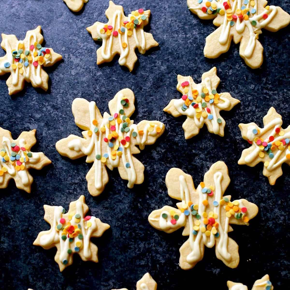 A bunch of snowflake shaped cookies with colored sprinkles.