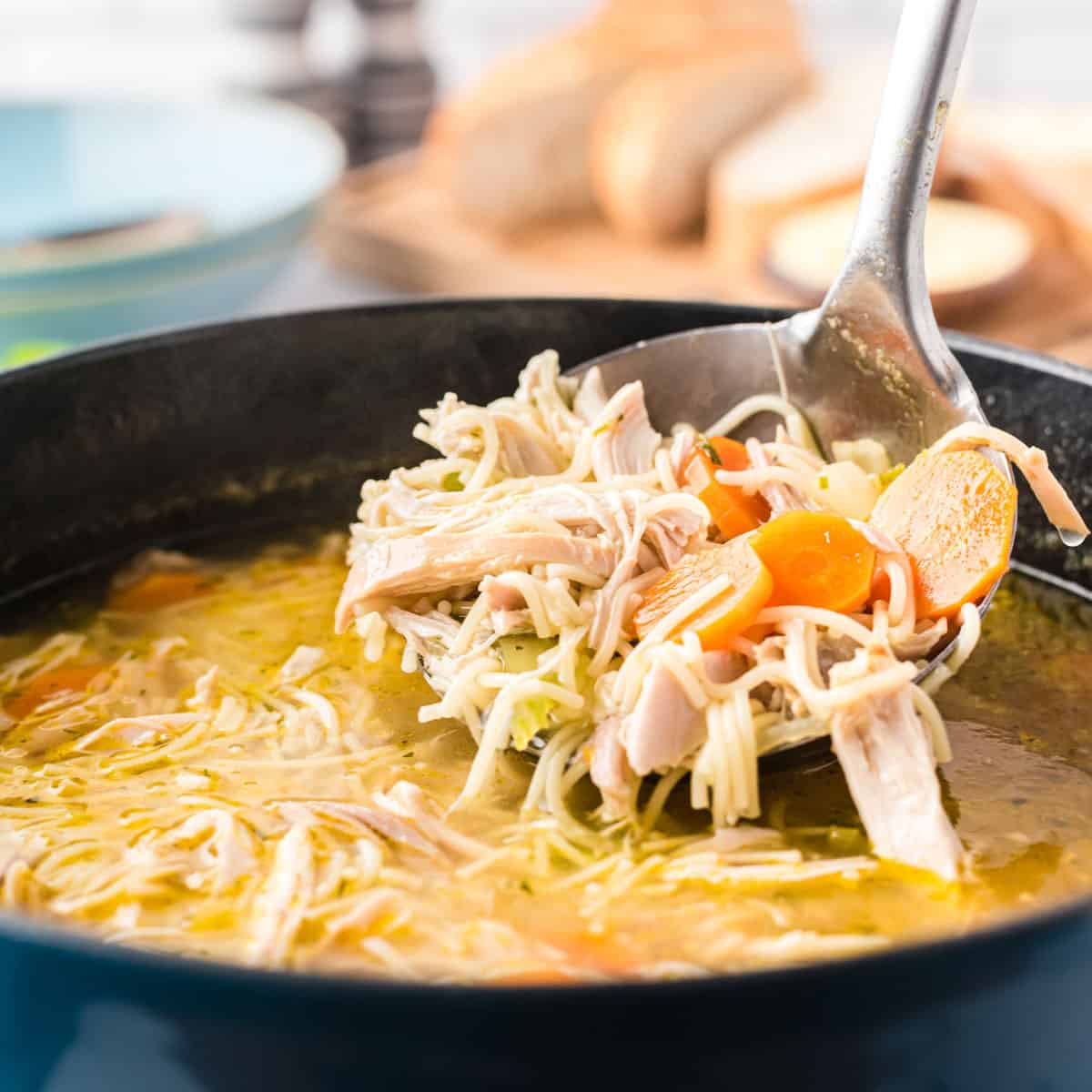 A large ladle of chicken noodle soup with chunks of carrots.