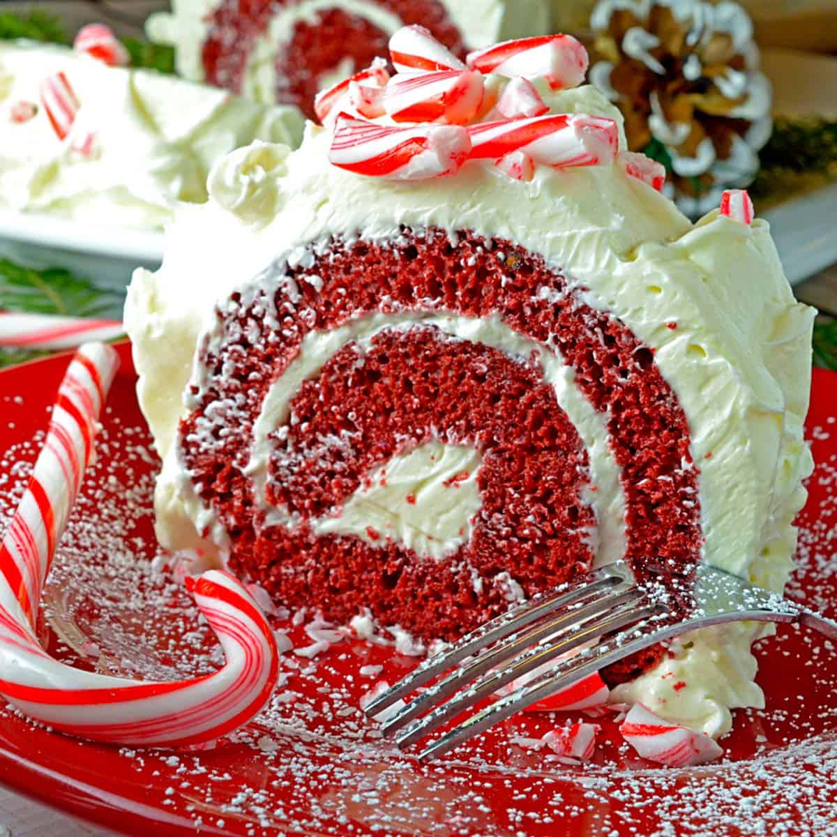 A serving of a red velvet cake roll and a candy cane on a red plate.
