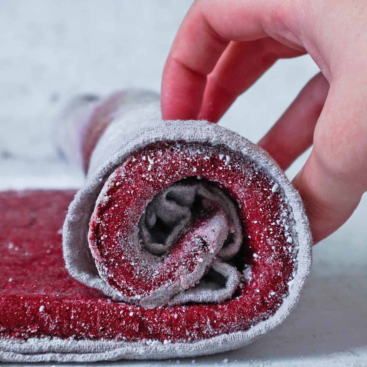 Rolling a red velvet cake in a clean kitchen towel with powdered sugar.