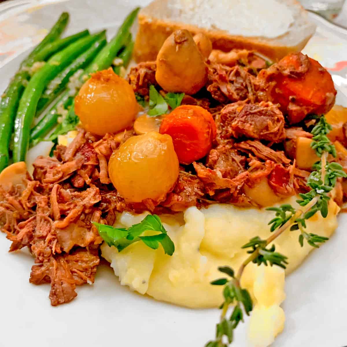 Beef stew over mashed potatoes with green beans.