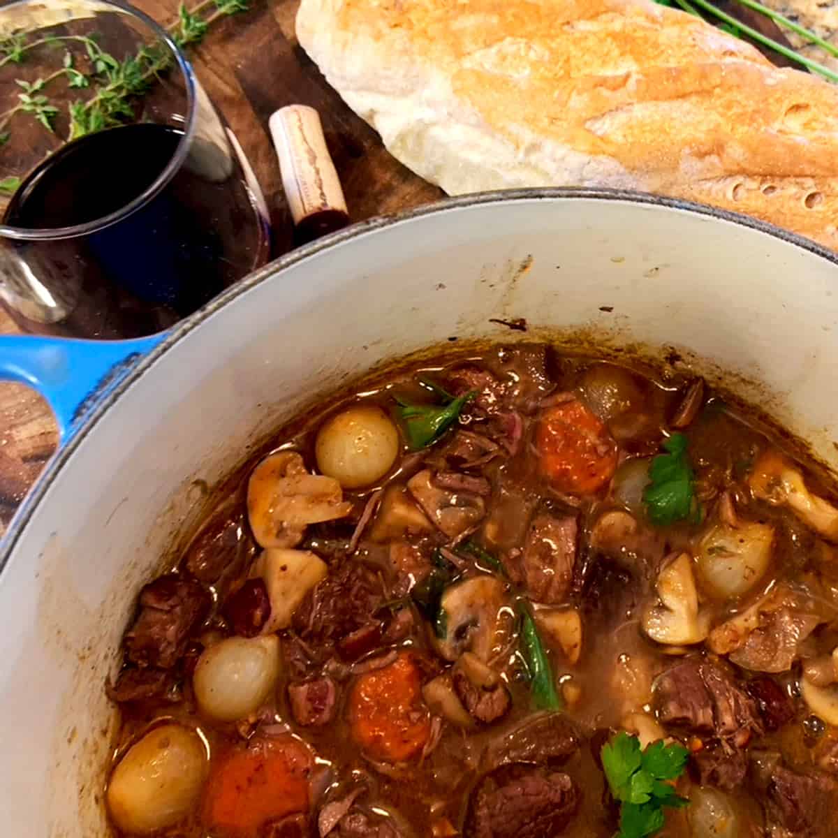 A pot of beef bourguignon with bread and red wine.